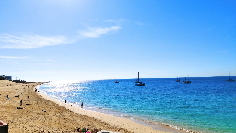 Breiter Sandstrand am Meer mit vielen Badegästen, die im Wasser und am Ufer unterwegs sind – ein stark frequentiertes Gebiet, in dem durch Bewegung, Sonne und Wasser jedes Jahr zahlreiche Münzen und Schmuckstücke verloren gehen.
