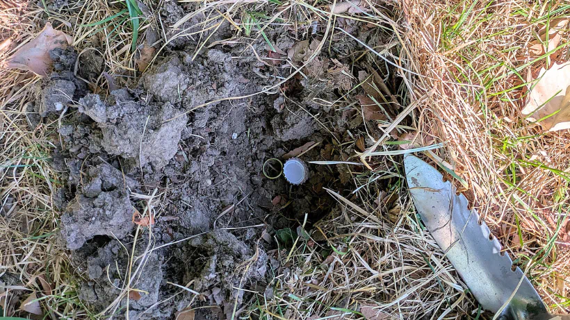 Ausgegrabene Funde im Erdreich: ein Kronkorken und ein Ring liegen in einer kleinen Grabung neben einem Sondelwerkzeug – zeigt, dass auch vermeintlich „schlechte“ Signale wertvolle Funde enthalten können.