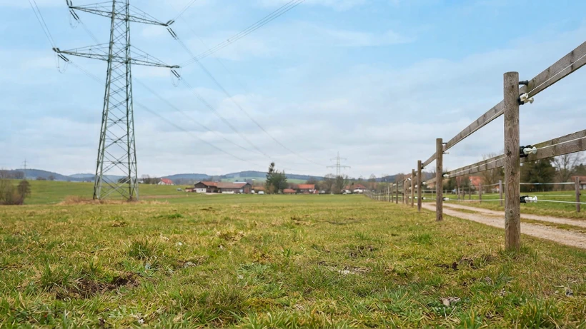 Landschaft mit Hochspannungsleitung, Weidezaun und nahen Gebäuden – typische Störquellen, die Metalldetektoren Geistersignale und instabile Leitwerte verursachen können.
