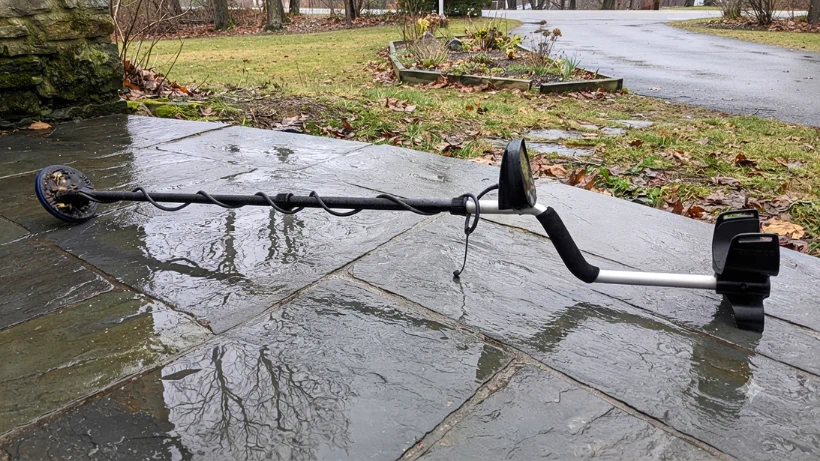 Teknetics Eurotek Pro (LTE) Metalldetektor auf nassem Steinweg im Park – robuste Outdoor‑Tauglichkeit bei feuchtem Wetter und wechselnden Suchbedingungen