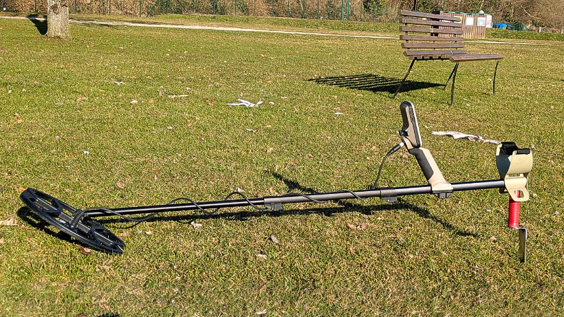 Metalldetektor mit Spule und Grabungswerkzeug auf einer Wiese – ideal für Testberichte und Praxisvergleiche.