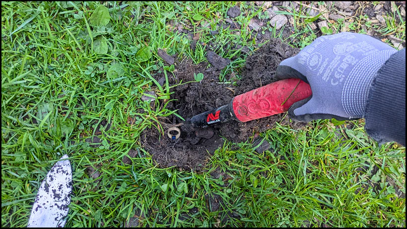 Sondler hebt im Gras einen Erdplug aus und legt einen Ring frei, um den Pinpointer im realen Praxistest draußen zu prüfen.